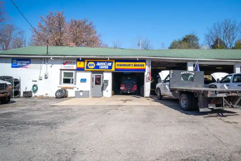 Wide-angle view of Schindler's Garage, showing the exterior facade, parking area, and green surroundings.