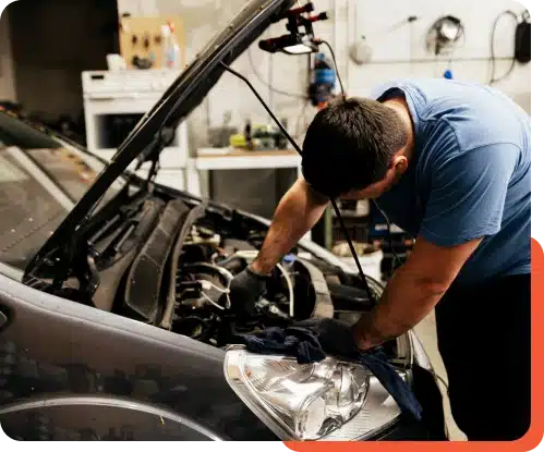 Technician at Schindler's Garage performing vehicle maintenance, inspecting under the hood with tools and diagnostic equipment nearby.