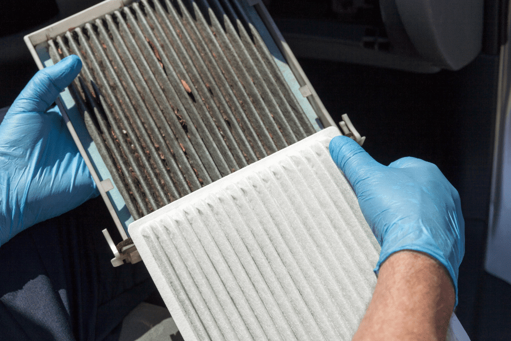 cabin air filter replacement, auto repair in Floyds Knobs, IN at Schindler's Garage. Technician wearing blue gloves holding a dirty cabin air filter with a clean replacement.