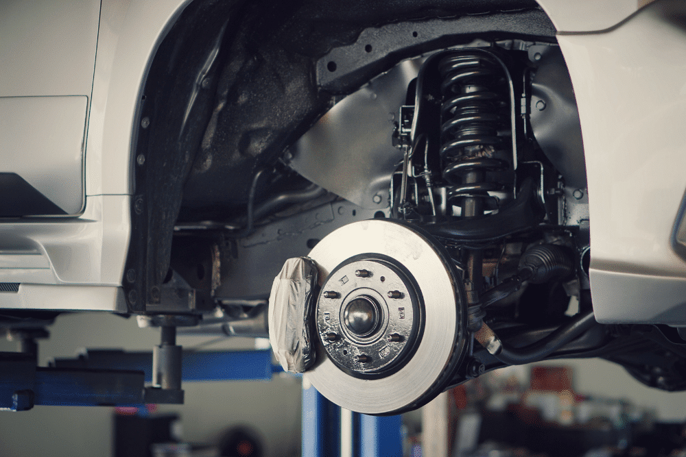 brake line repair, auto repair in Floyds Knobs, IN at Schindler's Garage. Close-up of a vehicle’s suspension and brake system, highlighting the brake rotor, caliper, and coil spring