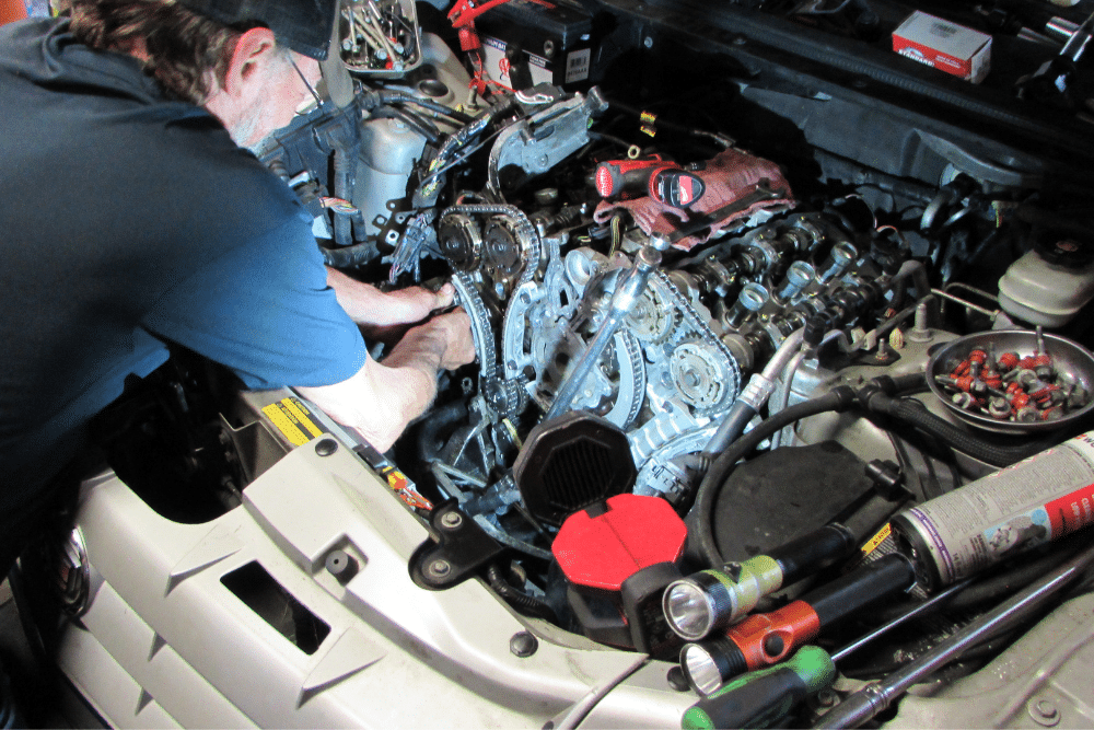 Scheduled maintenance in Floyds Knobs, IN at Schindler's Garage. A mechanic working on a car engine with exposed timing chains and tools around the engine bay.