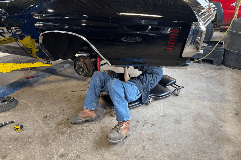 Spring car maintenance, auto repair in Floyds Knobs, IN by Schindler’s Garage. Image of a technician working beneath a lifted classic muscle car in a professional auto repair shop, highlighting skilled maintenance, restoration support, and dependable automotive care.