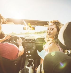 Summer Maintenance for your ford by Schindler's Garage in Floyds Knobs, IN: A couple enjoying a road trip in a convertible, driving down a sunny road, illustrating the importance of summer car maintenance for a smooth journey.