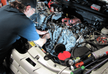 Car A/C Not Keeping Up With the Heat in Floyds Knobs, IN? Here's What's Really Happening - Schindler's Garage - Mechanic performing under-hood inspection while troubleshooting a vehicle air conditioning system.