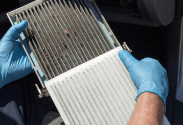 cabin air filter replacement, auto repair in Floyds Knobs, IN at Schindler's Garage. Technician wearing blue gloves holding a dirty cabin air filter with a clean replacement.