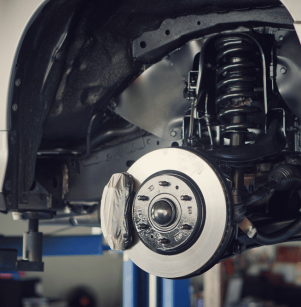 brake line repair, auto repair in Floyds Knobs, IN at Schindler's Garage. Close-up of a vehicle’s suspension and brake system, highlighting the brake rotor, caliper, and coil spring