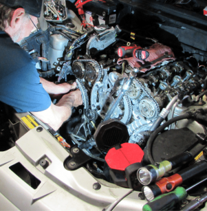 Scheduled maintenance in Floyds Knobs, IN at Schindler's Garage. A mechanic working on a car engine with exposed timing chains and tools around the engine bay.