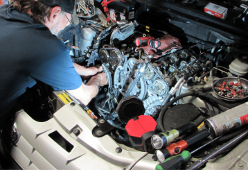 Scheduled maintenance in Floyds Knobs, IN at Schindler's Garage. A mechanic working on a car engine with exposed timing chains and tools around the engine bay.