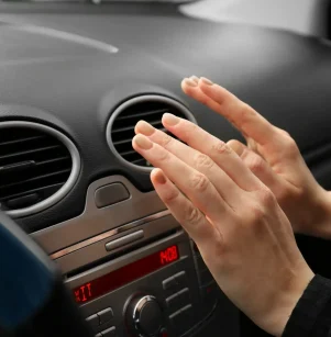 Auto AC Repair in Floyds Knobs, IN by Schindler’s Garage. Image of a woman checking the car air ventilation to understand why it is blowing hot air, indicating that the car needs to go to the AC repair shop