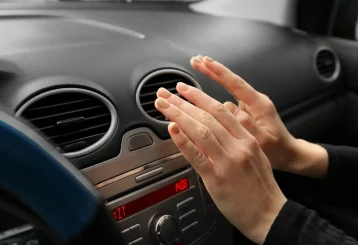 Auto AC Repair in Floyds Knobs, IN by Schindler’s Garage. Image of a woman checking the car air ventilation to understand why it is blowing hot air, indicating that the car needs to go to the AC repair shop